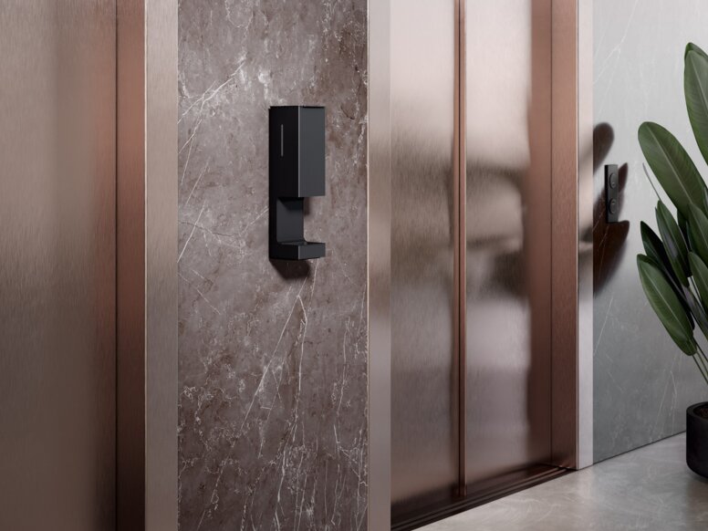 A touch-free disinfectant dispenser is installed on the wall between two lift doors